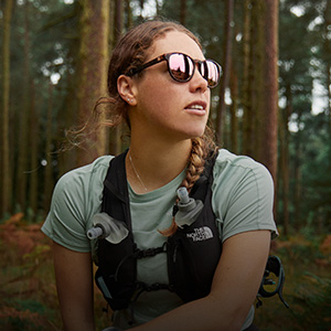 Shop accessories. A woman wearing sunglasses and running hydro vest is resting in woods
